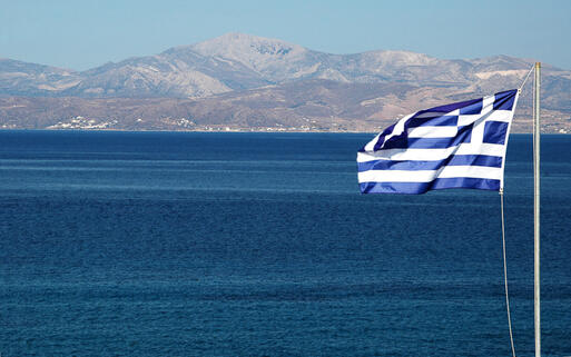Die griechische Flagge weht vor der Insel Naxos im Wind © rj lerich  / Shutterstock.com
